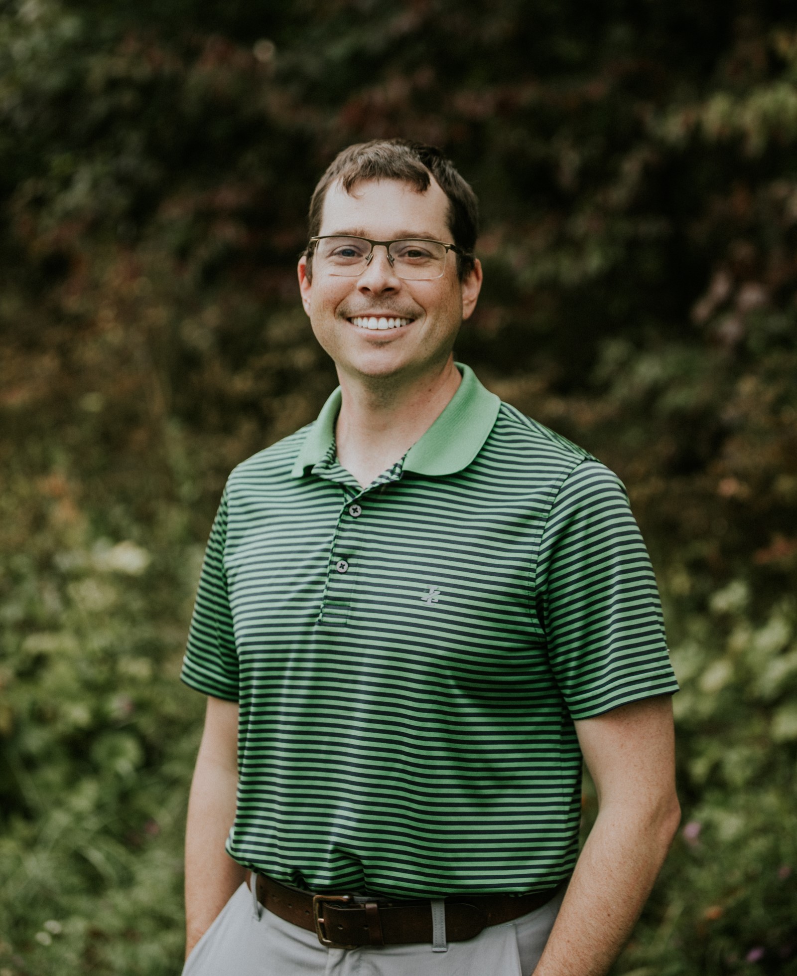 Headshot of man wearing glasses with trees in the background.